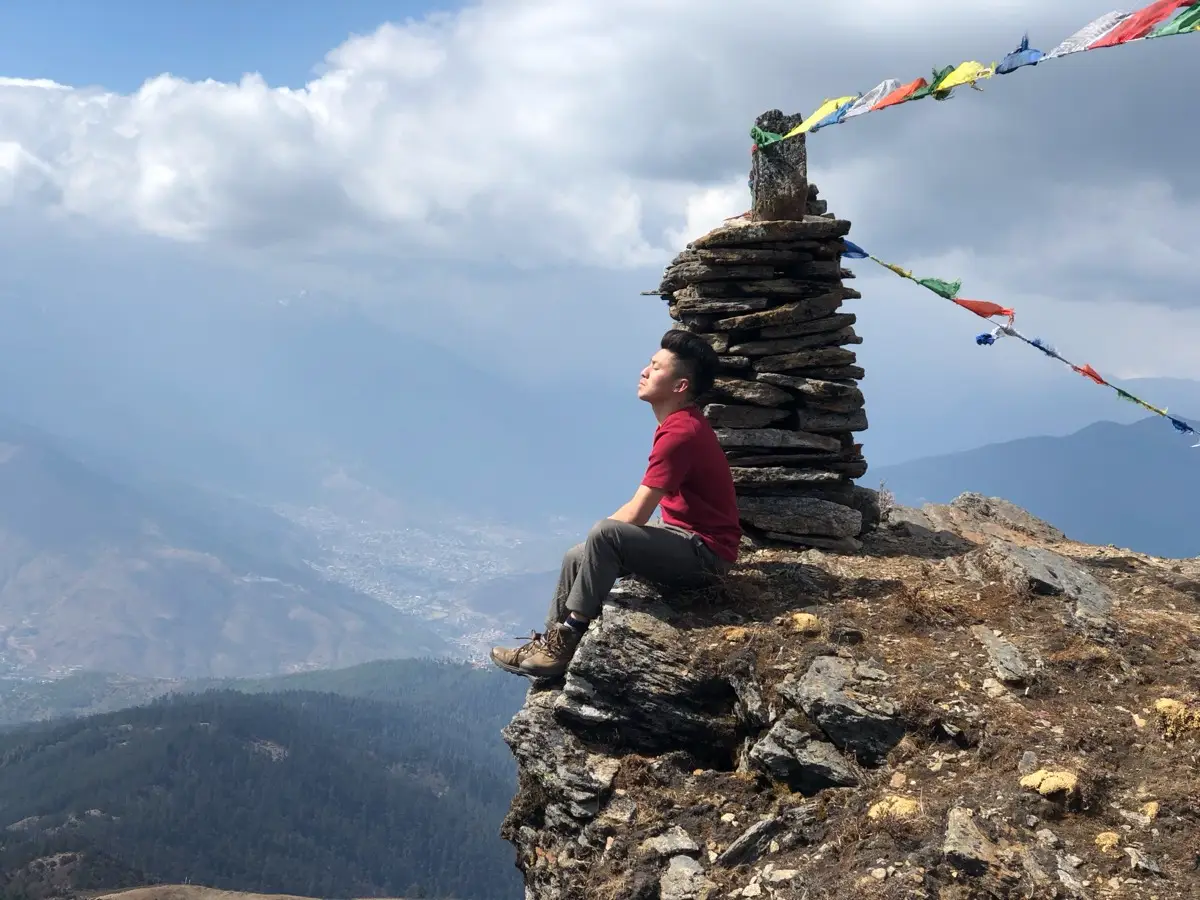 Traveller sitting in quiet reflection on a rocky outcrop above the clouds
